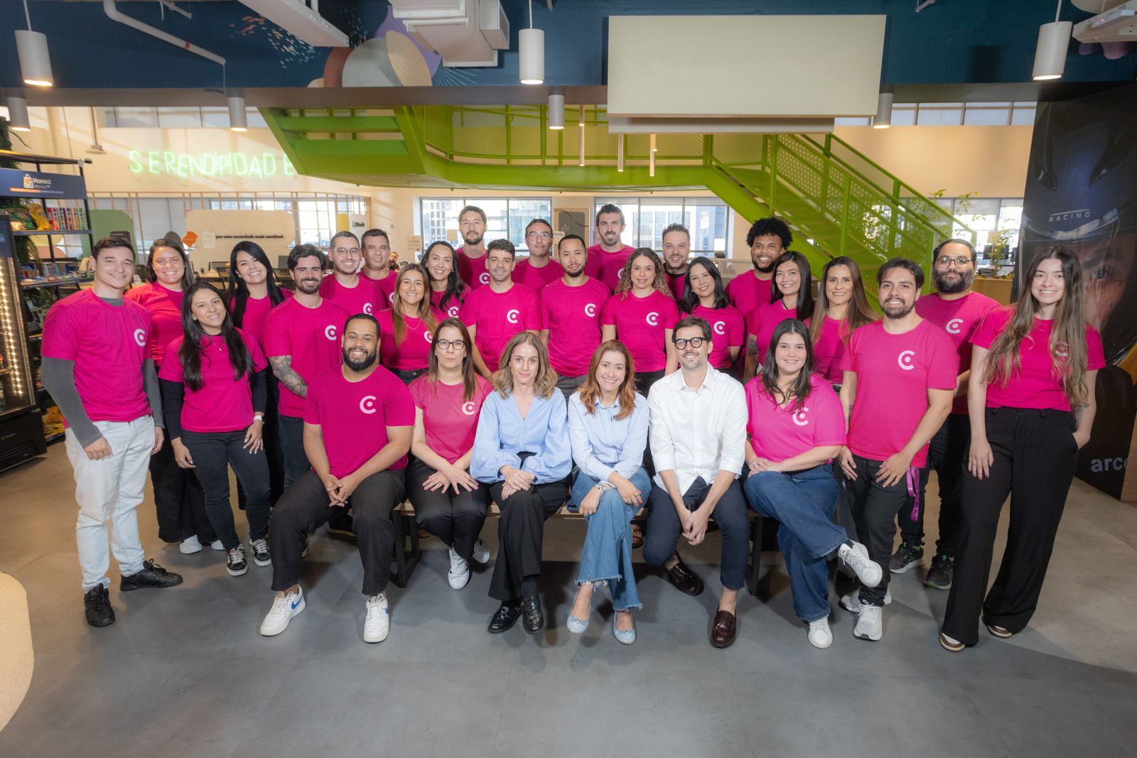 Equipe Cashin reunida em foto oficial no escritório Equipe da Cashin reunida para uma foto oficial, com colaboradores usando camisetas rosa com o logo da empresa, posando em um ambiente corporativo moderno.